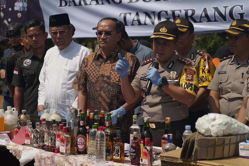 Wide shot of a group of officials standing behind a table covered in bottles.