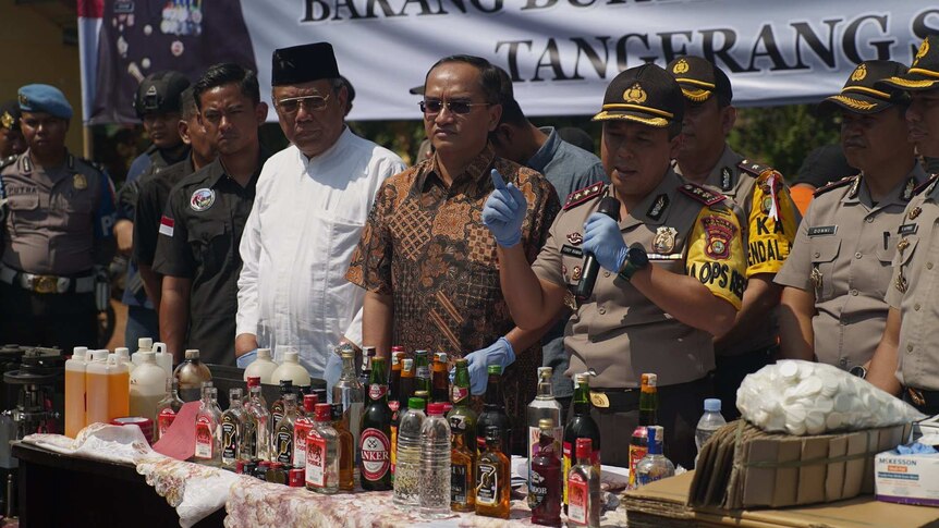 Wide shot of a group of officials standing behind a table covered in bottles.