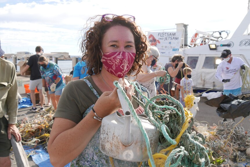 woman with curly hair, wearing a face mask holds on to an old kettle and pieces of old rope.