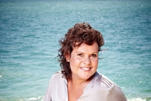 Tennis legend Evonne Goolagong-Cawley sits on a rock near the ocean.