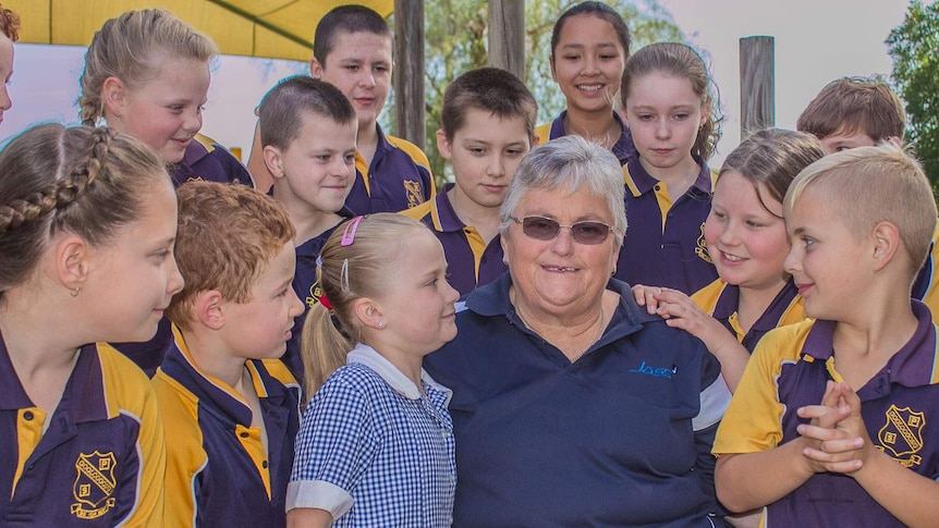 An older woman surrounded by children in school uniforms