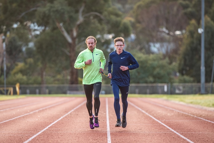 A wide photo shows Jaryd Clifford and Tim Logan jogging down the middle of the straight on an athletics track.