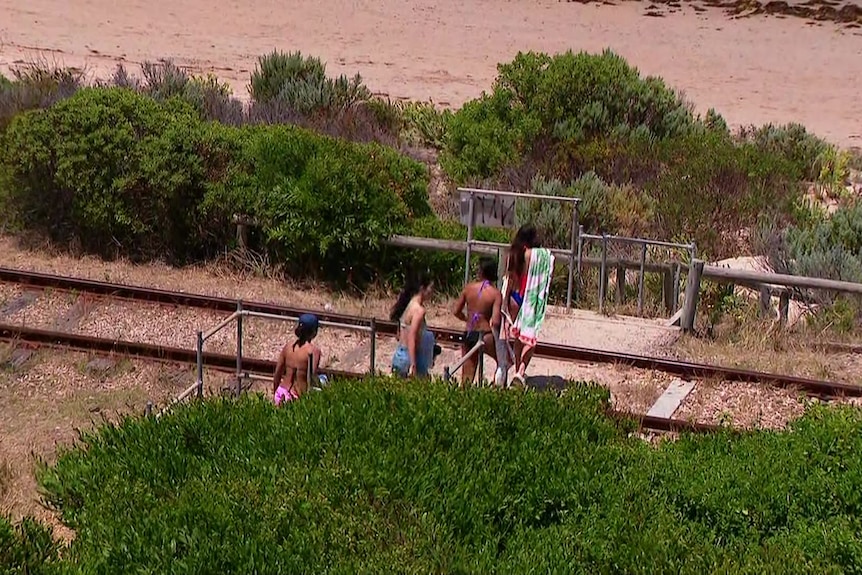 Beachgoers cross a railway line.