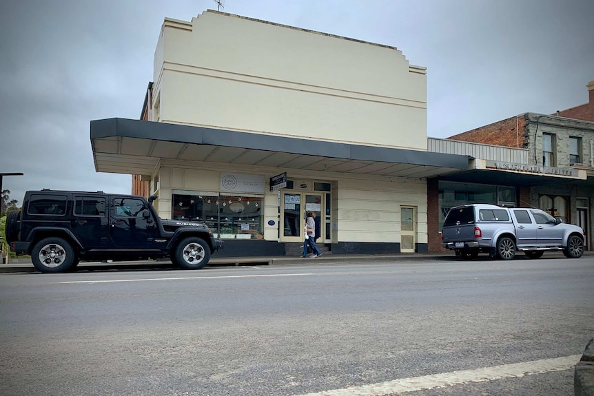 The outside of a white building with cars parked on the street on a grey day.