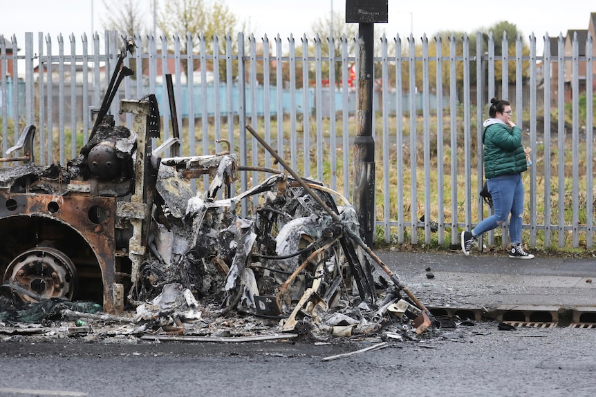 A woman walks past a burnt out bus in Belfast