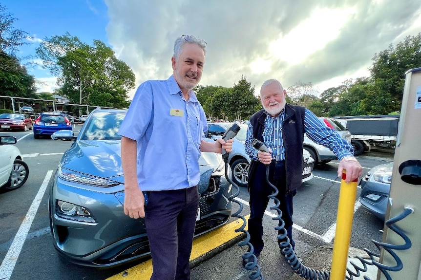 Two men standing in a car park holding two electric vehicle charging leads