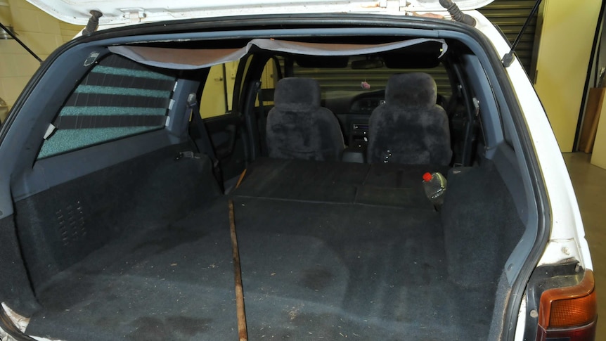 The open boot inside a white car parked in a room, which appears to be some kind of lab.