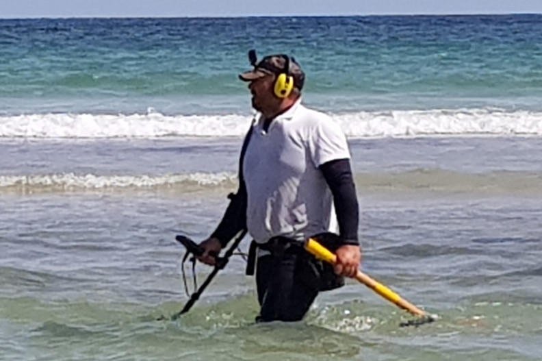 A man with a metal detector in shallow water at the beach