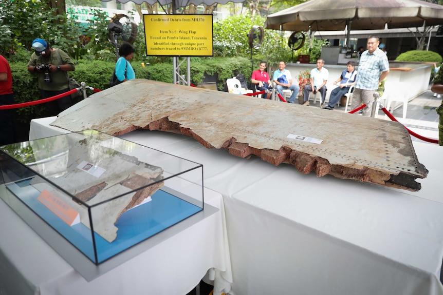 A large piece of debris from the missing Malaysia Airlines Flight is displayed alongside a smaller piece in a glass cabinet.