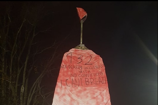 A monument with a fabric sign draped over it detailing the slaughter of Indigenous people.