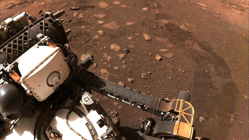 an image of NASA's Perseverance rover on Mars with track marks on red dirt