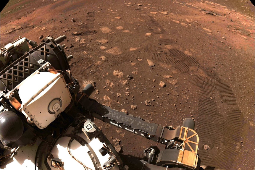 an image of NASA's Perseverance rover on Mars with track marks on red dirt
