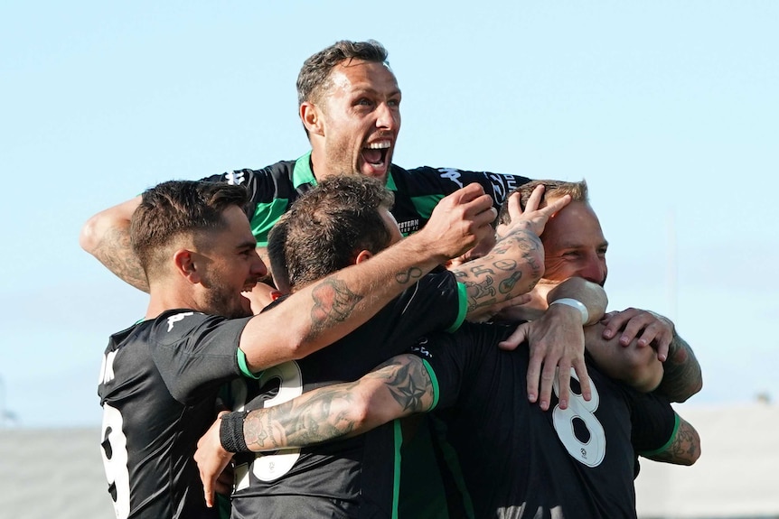 Western United players hug Panagiotis Kone (who can't be seen) after an A-League goal.