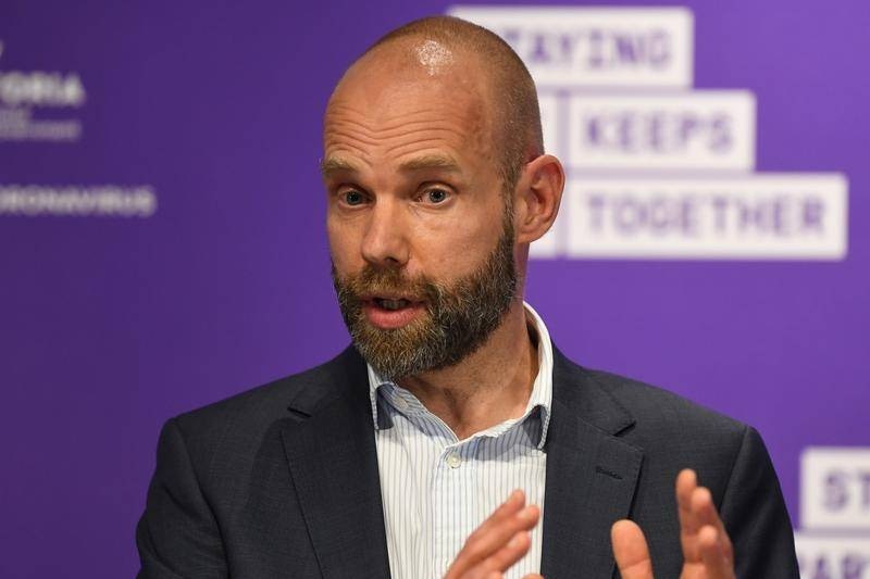 A lean, bald man with a neat beard, wearing a dark suit, gestures as he speaks at an official event.