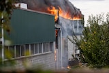 Flames erupt from the roof of a warehouse-like building.