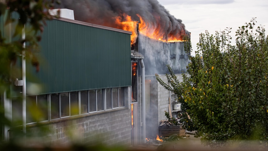 Flames erupt from the roof of a warehouse-like building.