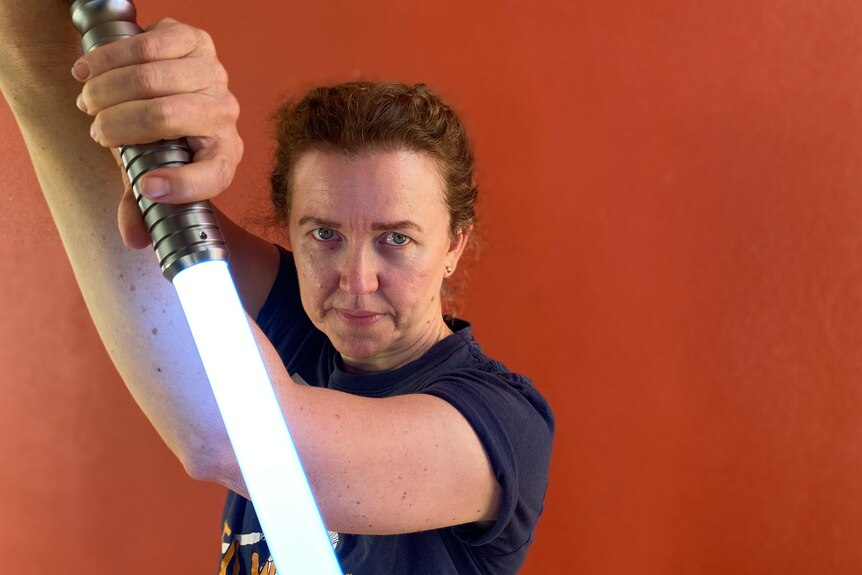 woman hold glowing blue lightsaber up to the camera 