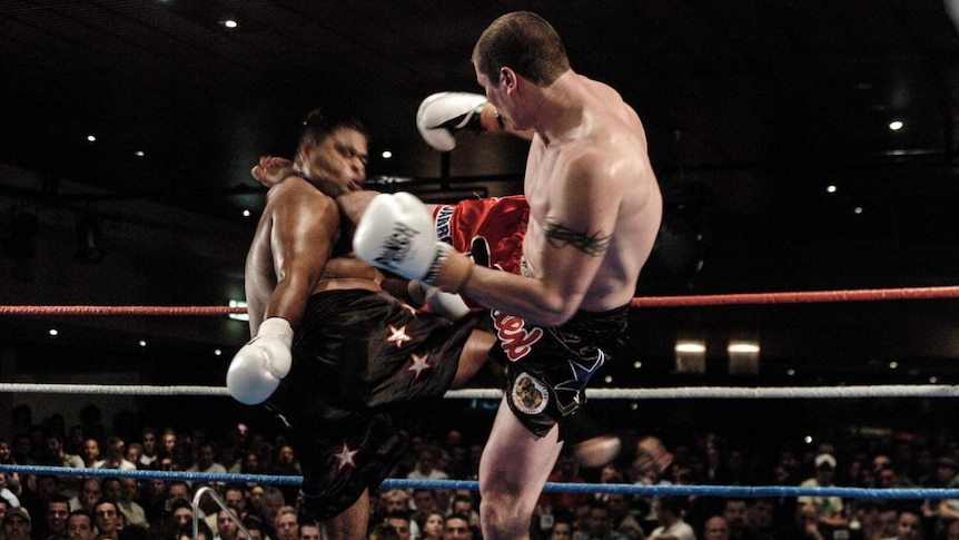 A man kicks a another man in the neck in a boxing ring.