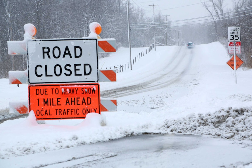 Road closed due to snow in Ohio. There is snow everywhere and the road is not visible except for car tyre tracks.