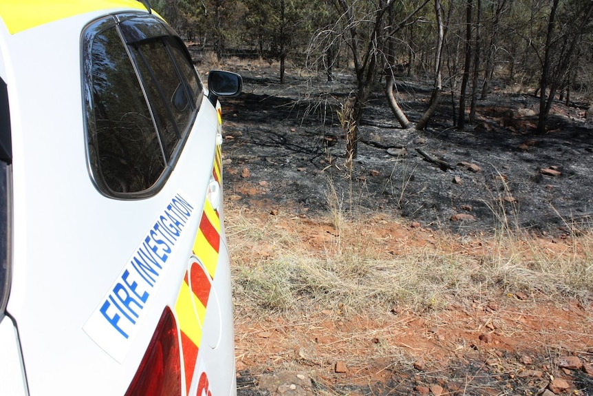 A car with a tag that says 'fire investigation' in front of a burnt paddock. 