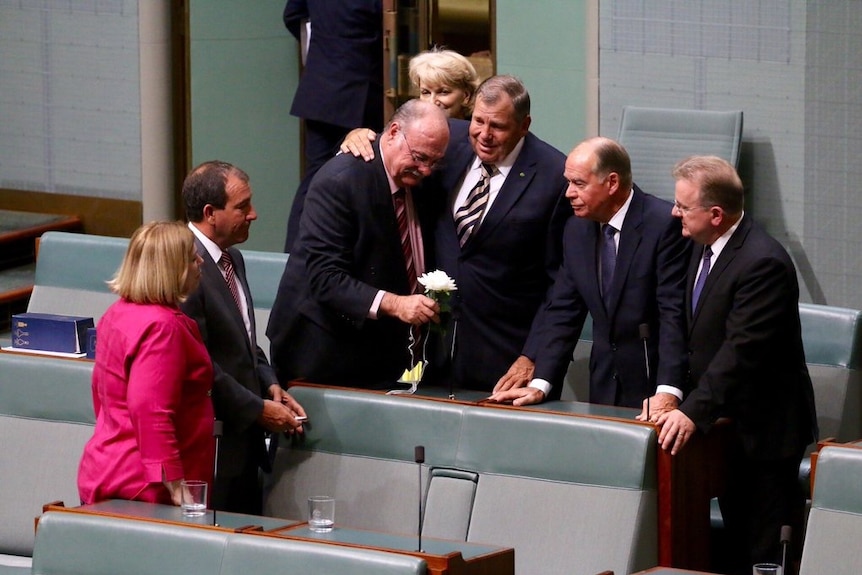 Warren Entsch in Parliament, holding a flower and surrounded by colleagues