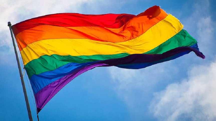 A flag with the colours of the rainbow flying on a flag post.