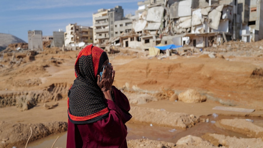 a woman covers her face with her hands and cries as she walks past destroyed buildings