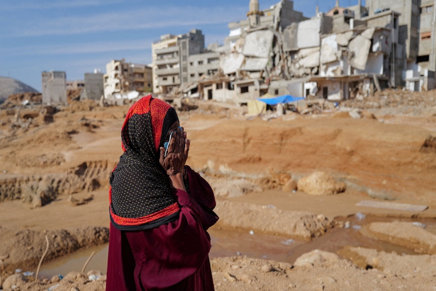 A woman covers her face with her hands and cries as she walks past destroyed buildings