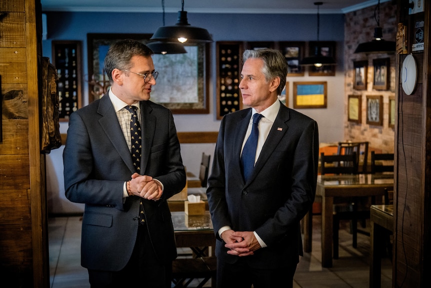 Two middle-aged men in suits stand and speak in a wood-panelled restaurant with the Ukrainian flag on the wall.