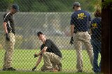 FBI technicians examine the outfield area of a baseball field.
