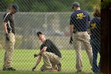 FBI technicians examine the outfield area of a baseball field.