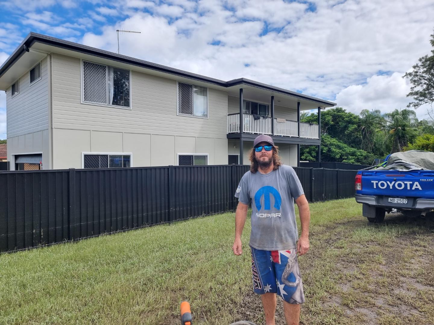A man standing outside his flooded house.
