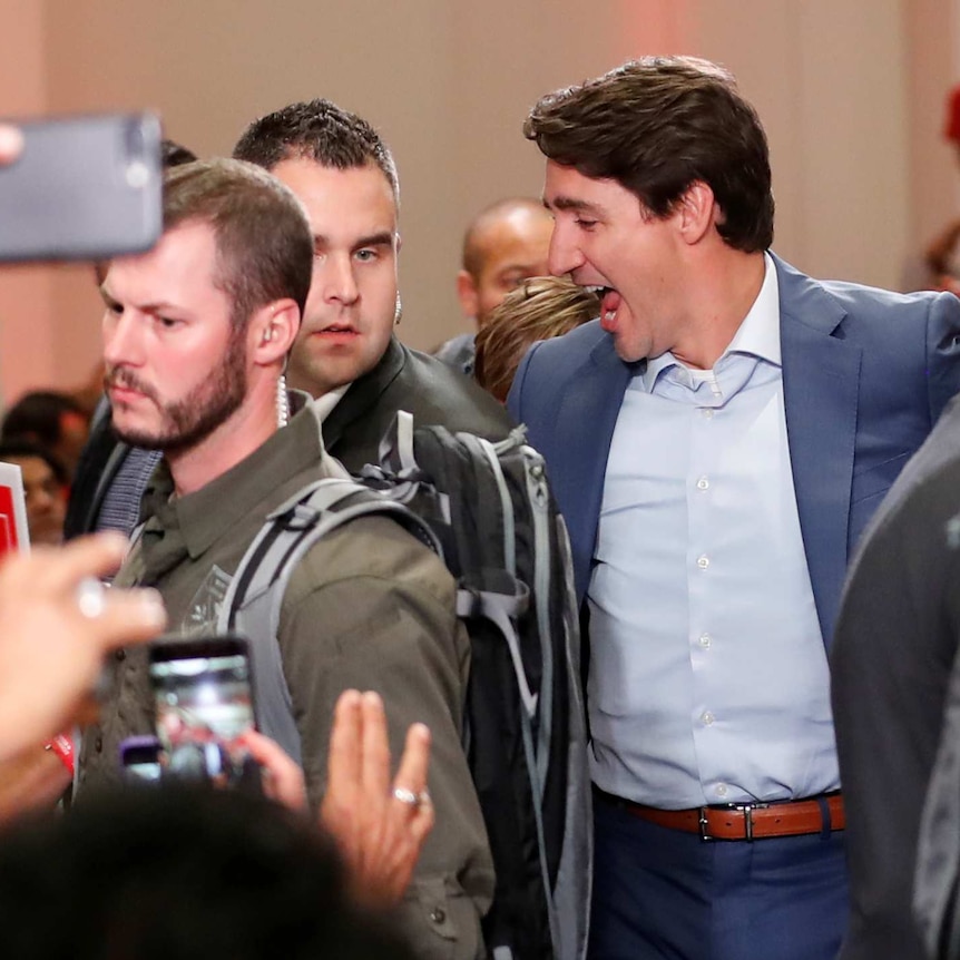 Justin Trudeau looks happy as he is surrounded  by security guards wearing army green