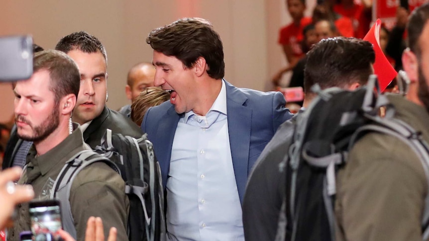 Justin Trudeau looks happy as he is surrounded  by security guards wearing army green