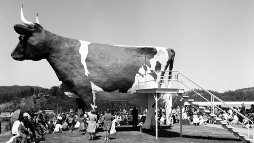 A big cow sculpture with lots of people around it