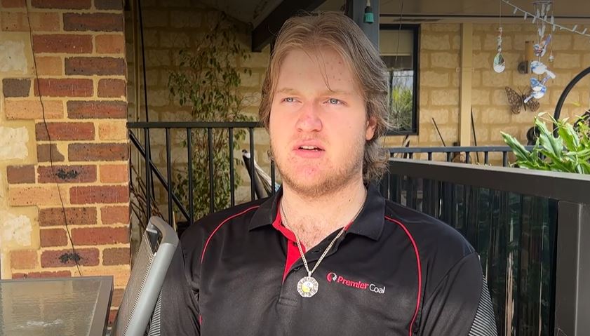 A young man in a black premier coal polo speaks into the camera.