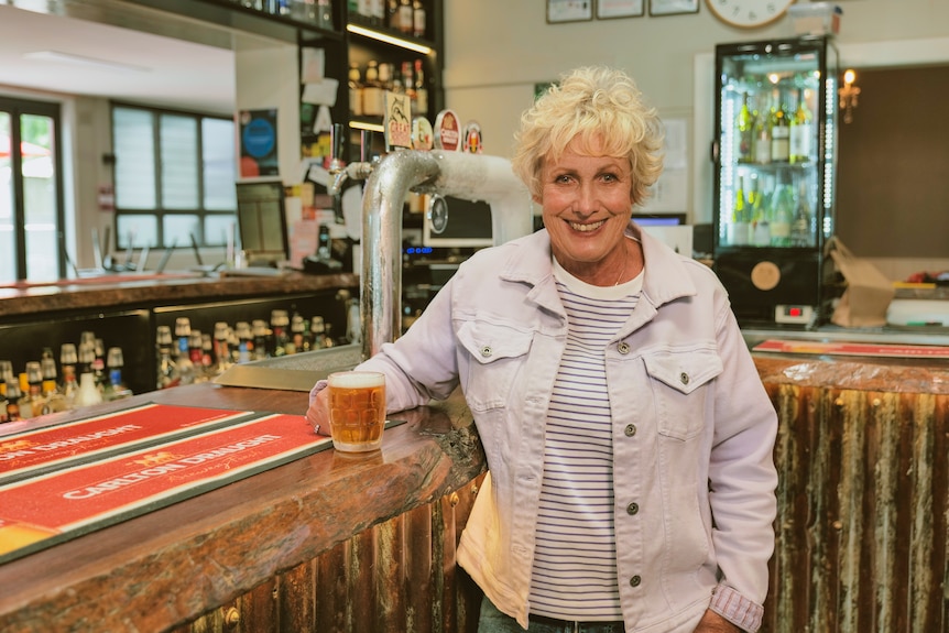 Woman standing at the bar in a pub holding a glass of beer and smiling. 