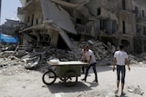 Man pushes cart near damaged buildings in Aleppo