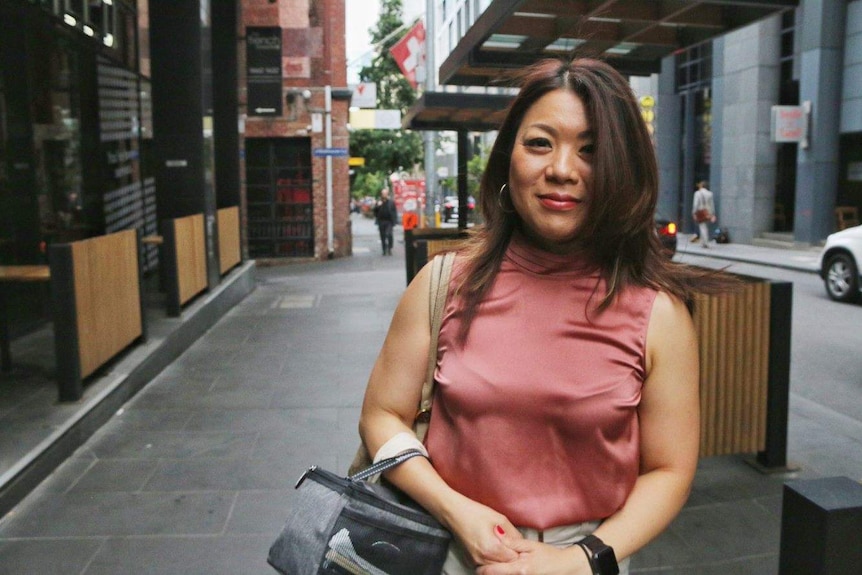 A woman in a pink top stands on an inner city street in Melbourne looking at the camera.