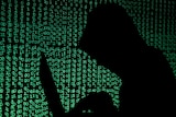 A hooded man holds a laptop computer as cyber code is projected on him in this illustration picture