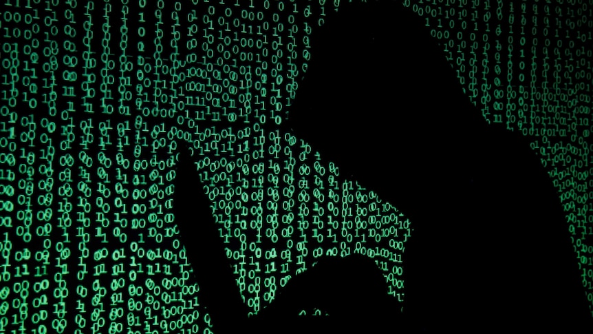 A hooded man holds a laptop computer as cyber code is projected on him in this illustration picture