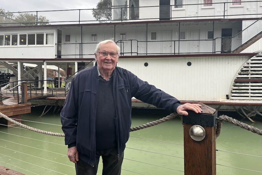 A happy man stands in front of a paddle-steamer.
