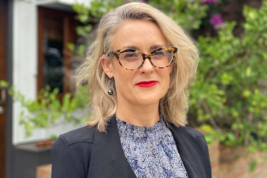 A woman wearing glasses stands in a garden