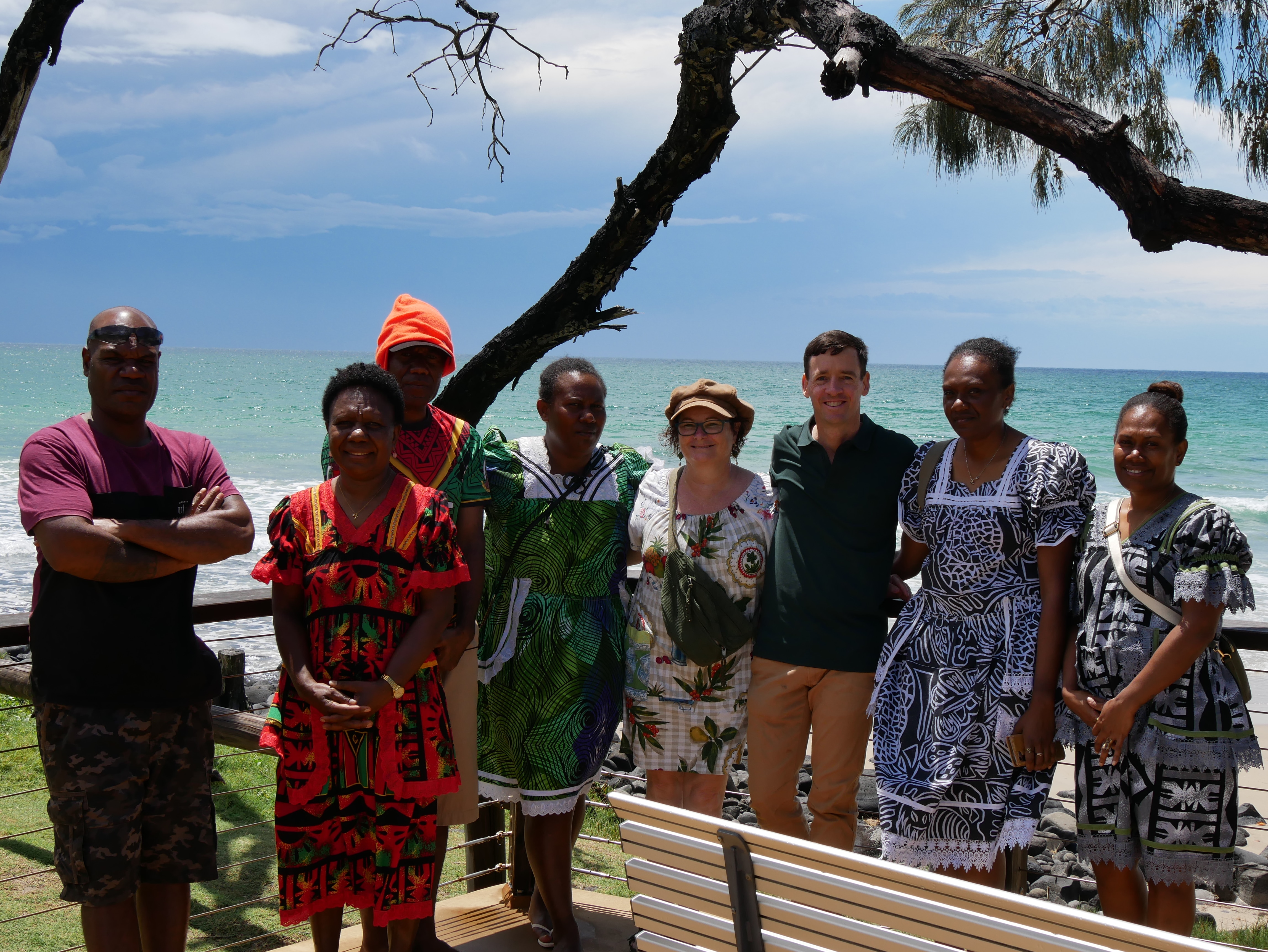 Un grupo de personas paradas juntas y sonriendo a la cámara con el mar detrás de ellos.