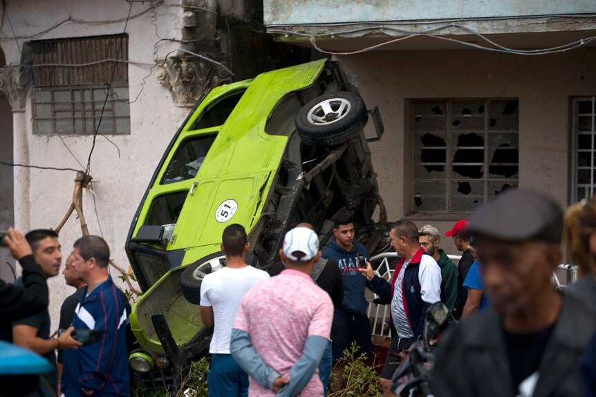People stand around a green car flipped by the Havana tornado