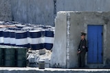 A North Korean soldier stands guard over a stockpile of oil barrels.