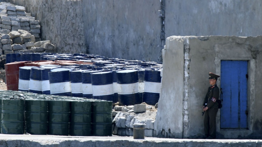 A North Korean soldier stands guard over a stockpile of oil barrels.
