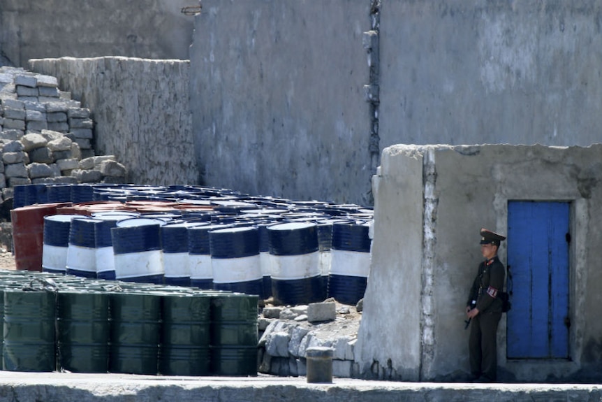 A North Korean soldier stands guard over a stockpile of oil barrels.