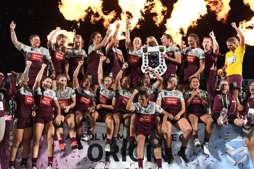 A group of women celebrating with the shield after winning an interstate game of rugby league 