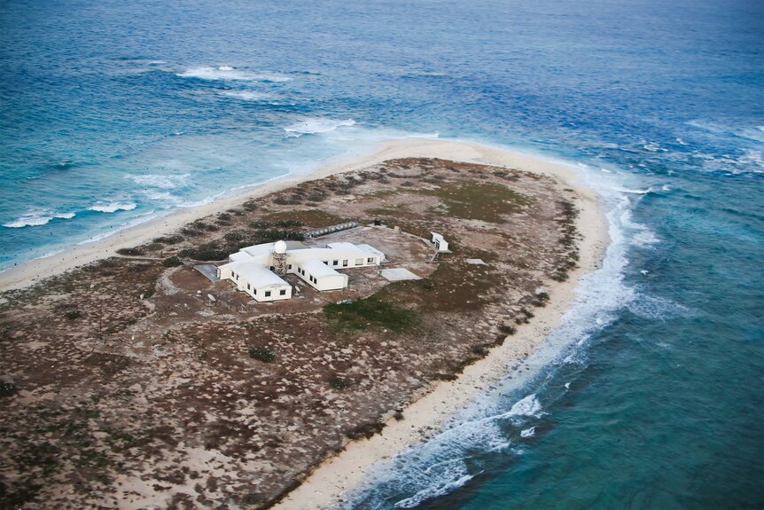 An aerial shot of a building on a tiny island surrounded by ocean